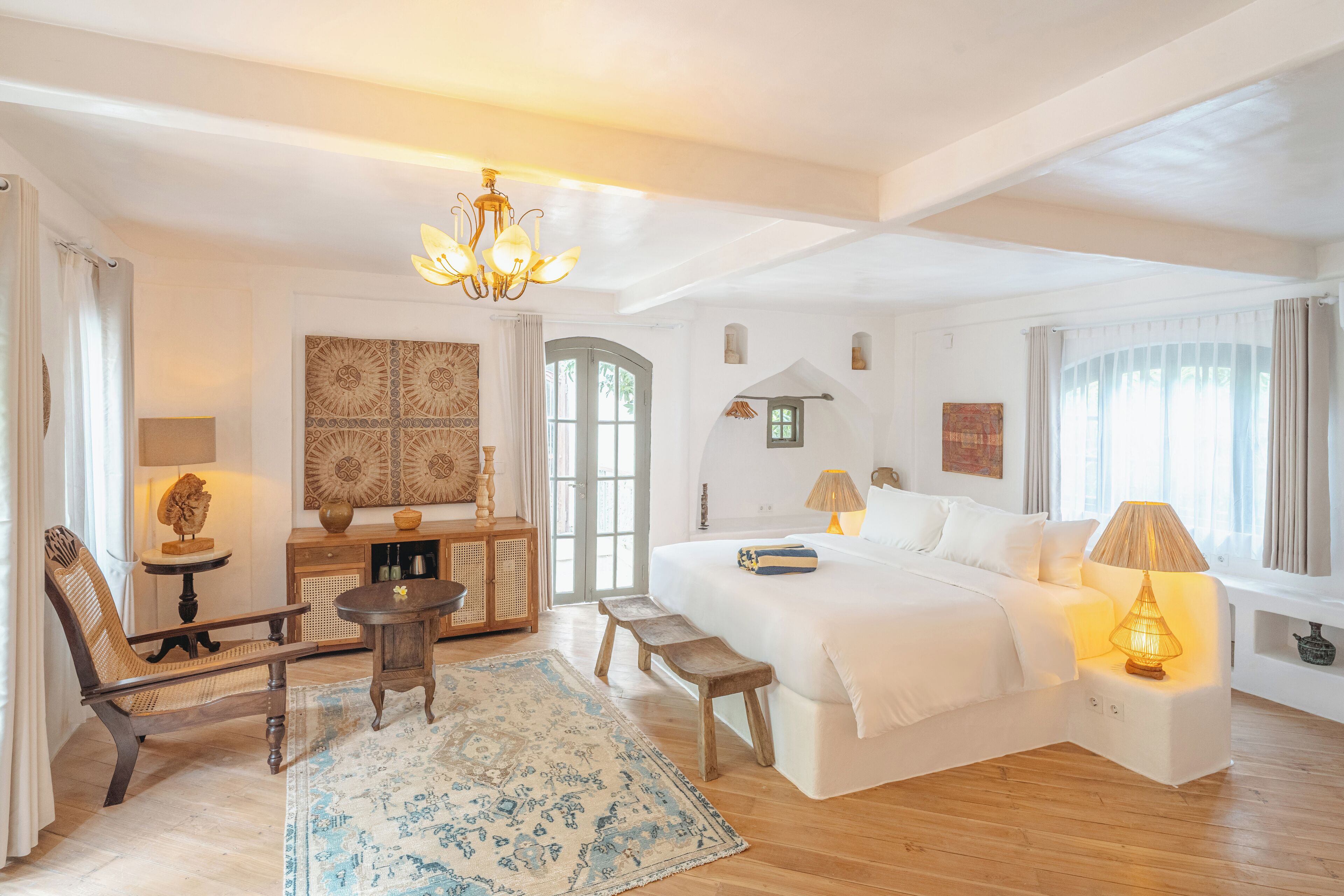 A spacious bedroom with a large bed, a wooden bench, a small table, and a chandelier.