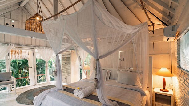 A bedroom with a canopy bed, a bedside table with a lamp, and a view of the outdoors. - La Santa Rosa (Jimbaran)