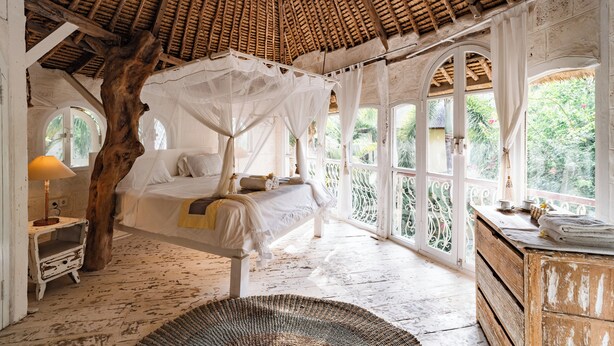 A room with a bed under a canopy, a wooden dresser, and large windows with a view of greenery. - La Santa Rosa (Jimbaran)