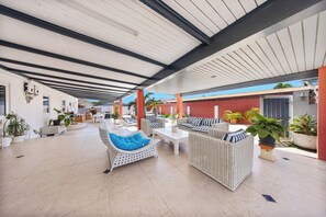 An open-air covered patio with wicker furniture and potted plants. - Oranjestad Retreat: 4BR Paradise with Private Pool (Oranjestad)