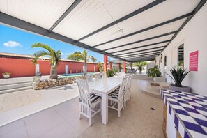 An outdoor patio with a white table and chairs, surrounded by potted plants and a red wall. - Oranjestad Retreat: 4BR Paradise with Private Pool (Oranjestad)