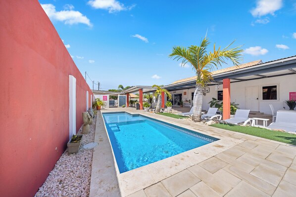 A swimming pool with a tiled deck, surrounded by lounge chairs and palm trees.
