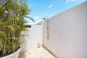 A small, enclosed outdoor shower area with a white wall, a potted plant, and a tiled floor. - Oranjestad Retreat: 4BR Paradise with Private Pool (Oranjestad)