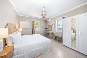 A bedroom with a bed, bedside table, desk, wardrobe, and a window with curtains. - Oranjestad Retreat: 4BR Paradise with Private Pool (Oranjestad)