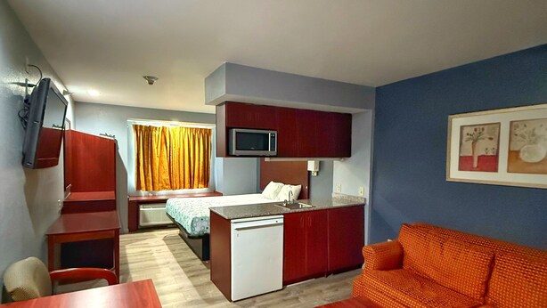 A compact hotel room with a kitchenette, a bed, a sofa, and a dining table.