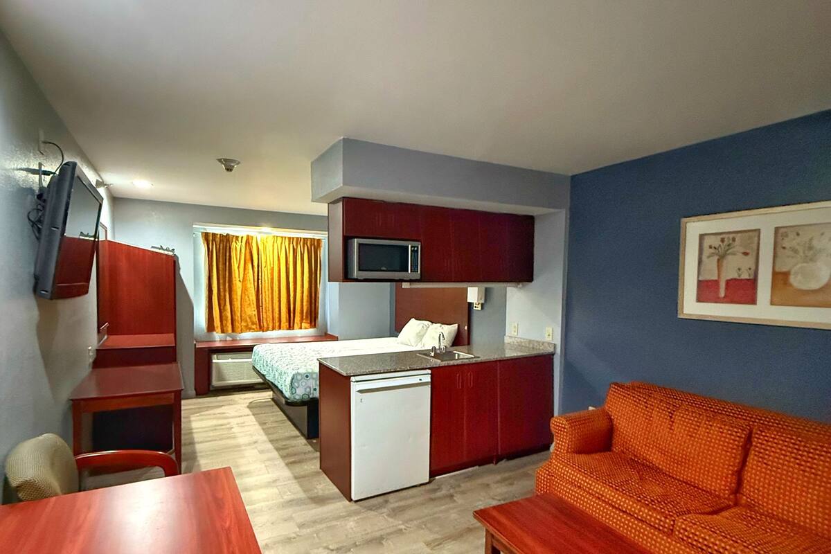 Habitación de hotel compacta con kitchenette, una cama, un sofá y una mesa de comedor.