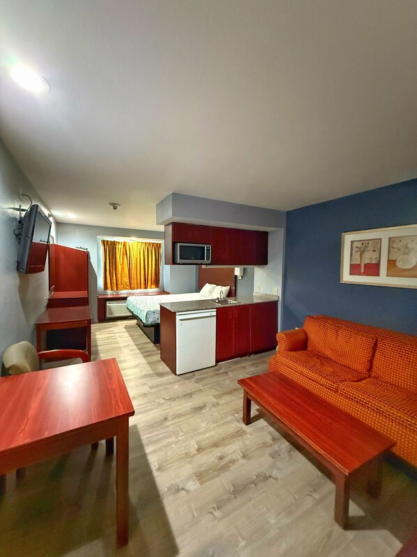 A compact hotel room with a kitchenette, a bed, a sofa, and a dining table.