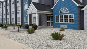 A multi-story hotel with a blue building in the foreground, a covered walkway, and a gravel driveway.