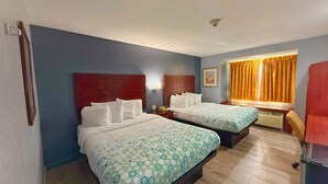 Une chambre d’hôtel avec deux lits, une tête de lit en bois, une fenêtre avec des rideaux et une table de chevet avec une lampe.