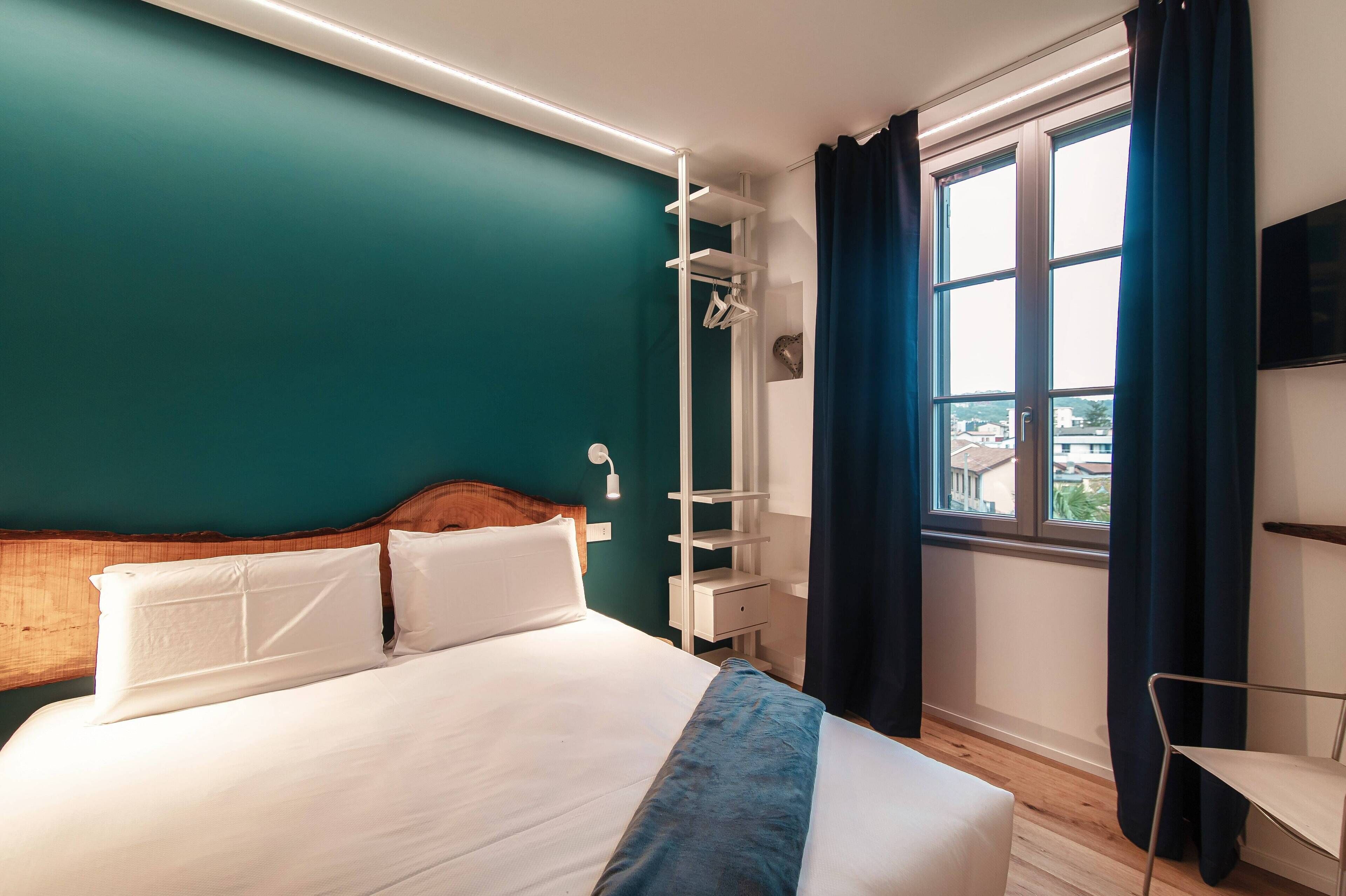 A hotel room with a bed, a wardrobe, a chair, and a TV on the wall.