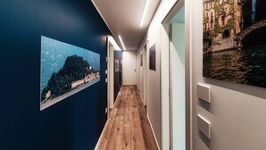 Een gang met houten vloer, witte wanden en kunstwerken die een landschap en een gebouw voorstellen.