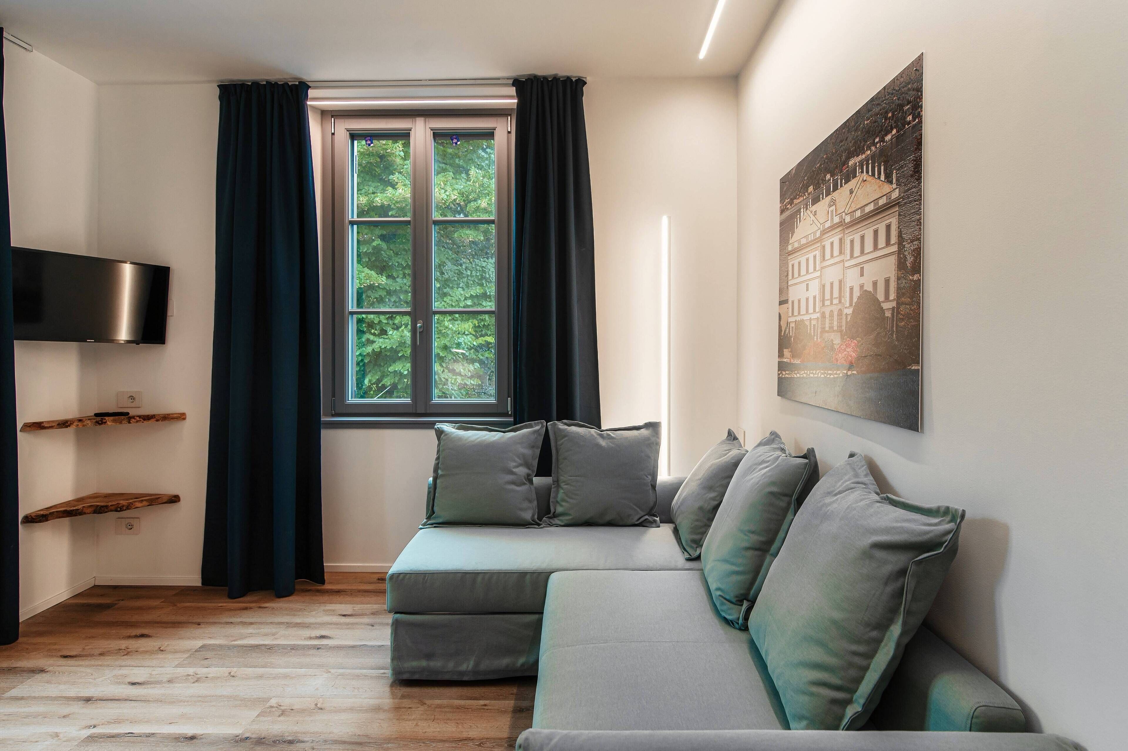 Una sala de estar moderna con un sofá modular, un televisor de pantalla plana montado en la pared y un ventanal con cortinas.