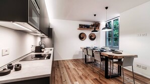Een moderne keuken met een centraal eiland, houten vloeren en een eethoek met een groot raam.