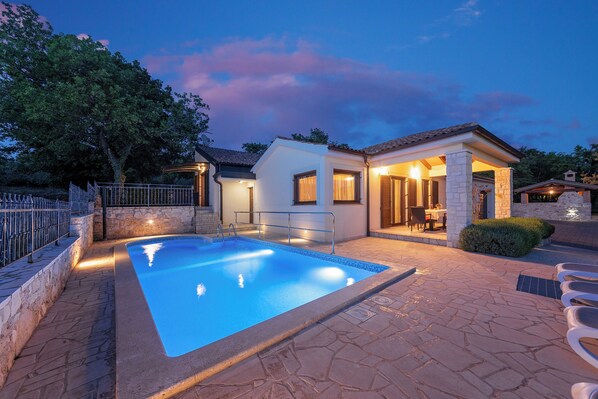 Relax by the serene pool surrounded by a beautifully maintained patio and a building with a stone facade.