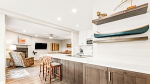 A modern kitchen with wooden cabinets, a white countertop, and a dining area with a chair and table. - Downtown Cozy Condo; Walk to town, Slopes & Hiking (Breckenridge)