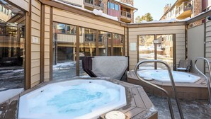 A spa area with two hot tubs and a sauna, surrounded by stone walls and large windows. - Downtown Cozy Condo; Walk to town, Slopes & Hiking (Breckenridge)