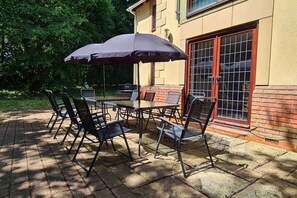 An outdoor patio with a table and chairs, a grill, and a large umbrella.