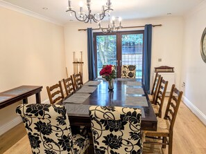 Ein Esszimmer mit einem langen Holztisch, stuhlförmigen Sitzgelegenheiten mit Blumenmuster, einer Chandelüstere und Blick durch eine Glastür.