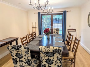 Una sala da pranzo con un lungo tavolo, sedie, un lampadario e vista panoramica attraverso una porta di vetro.