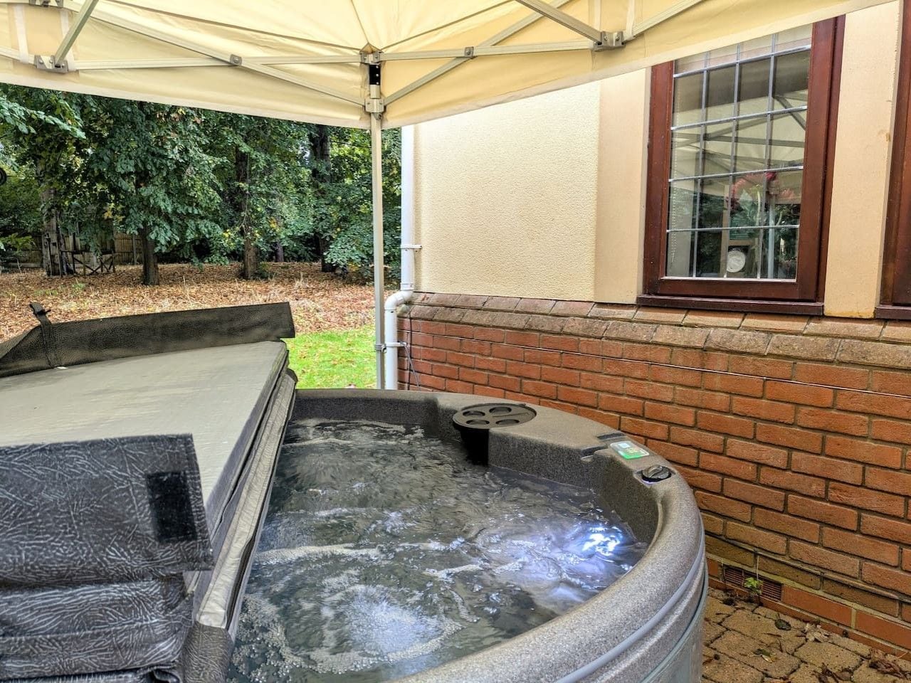 A hot tub with a canopy, a brick wall, and a window.