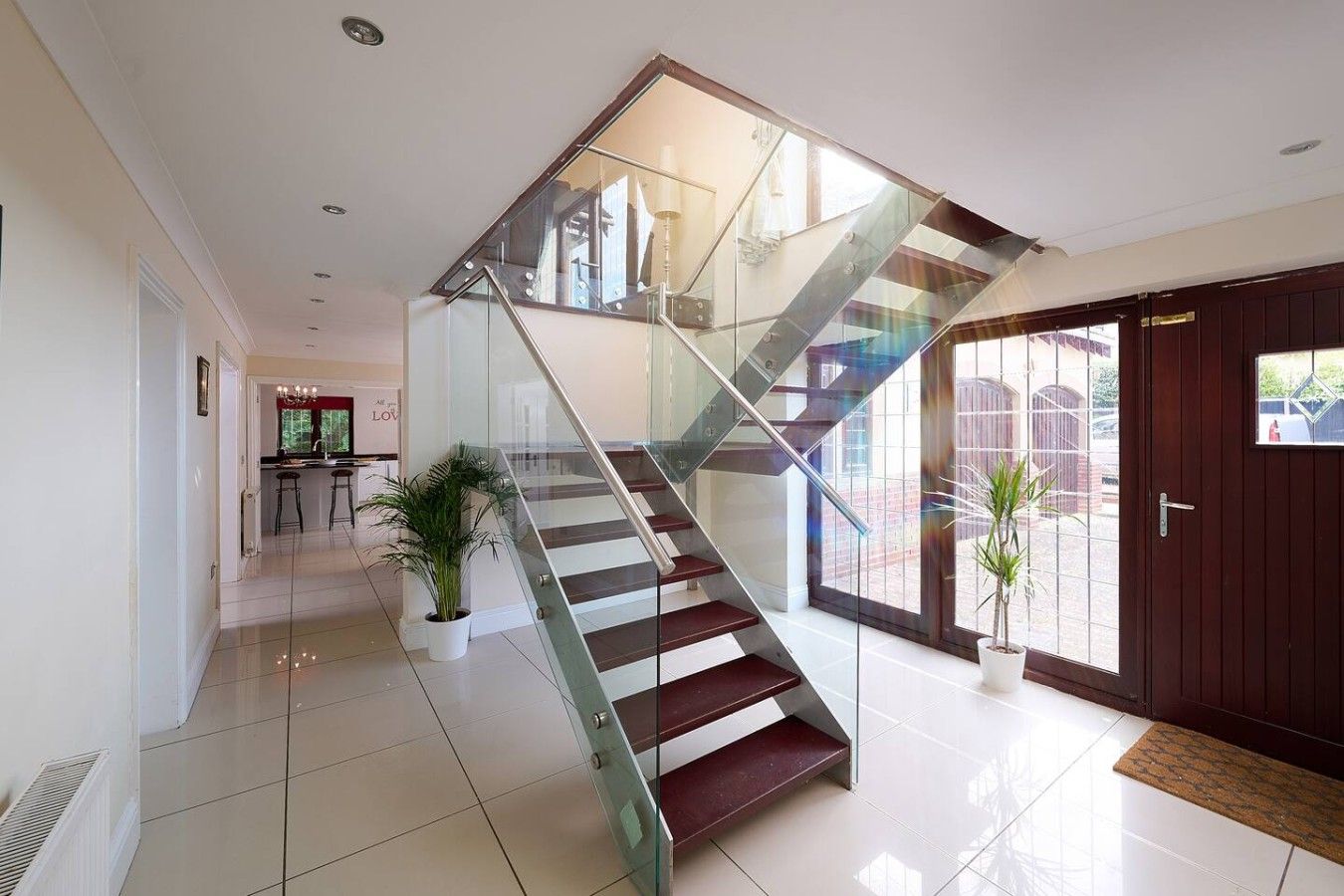 Un interior moderno con una escalera de cristal que lleva a un segundo piso, una zona de cocina y un amplio acceso por una puerta de cristal.