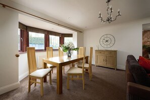 A dining room with a wooden table and chairs, a clock on the wall, and a view through the window. - Spacious 7BR Home, families & Contractors, Hot Tub (Wolverhampton)