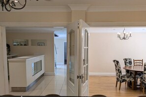 A dining area with a round table and patterned chairs, a kitchen with a white countertop, and a hallway leading to another room. - Spacious 7BR Home, families & Contractors, Hot Tub (Wolverhampton)