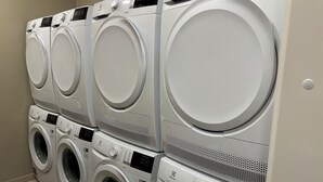 A row of white, stacked front-loading washing machines in a laundry room. - Frost Apartments by Heimaleiga (Reykjavik)