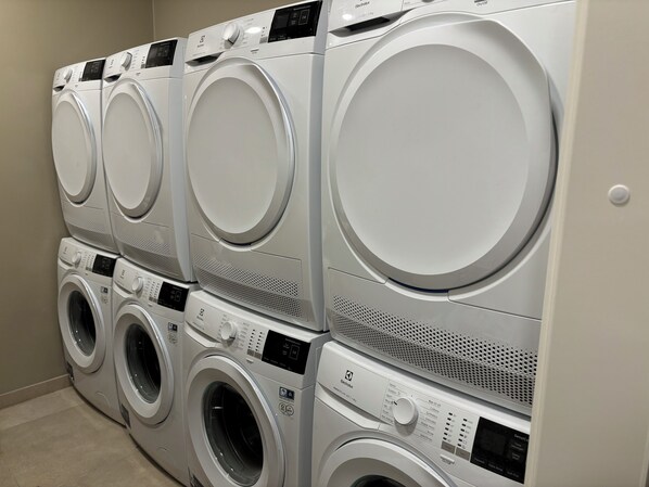 A row of white, stacked front-loading washing machines in a laundry room.