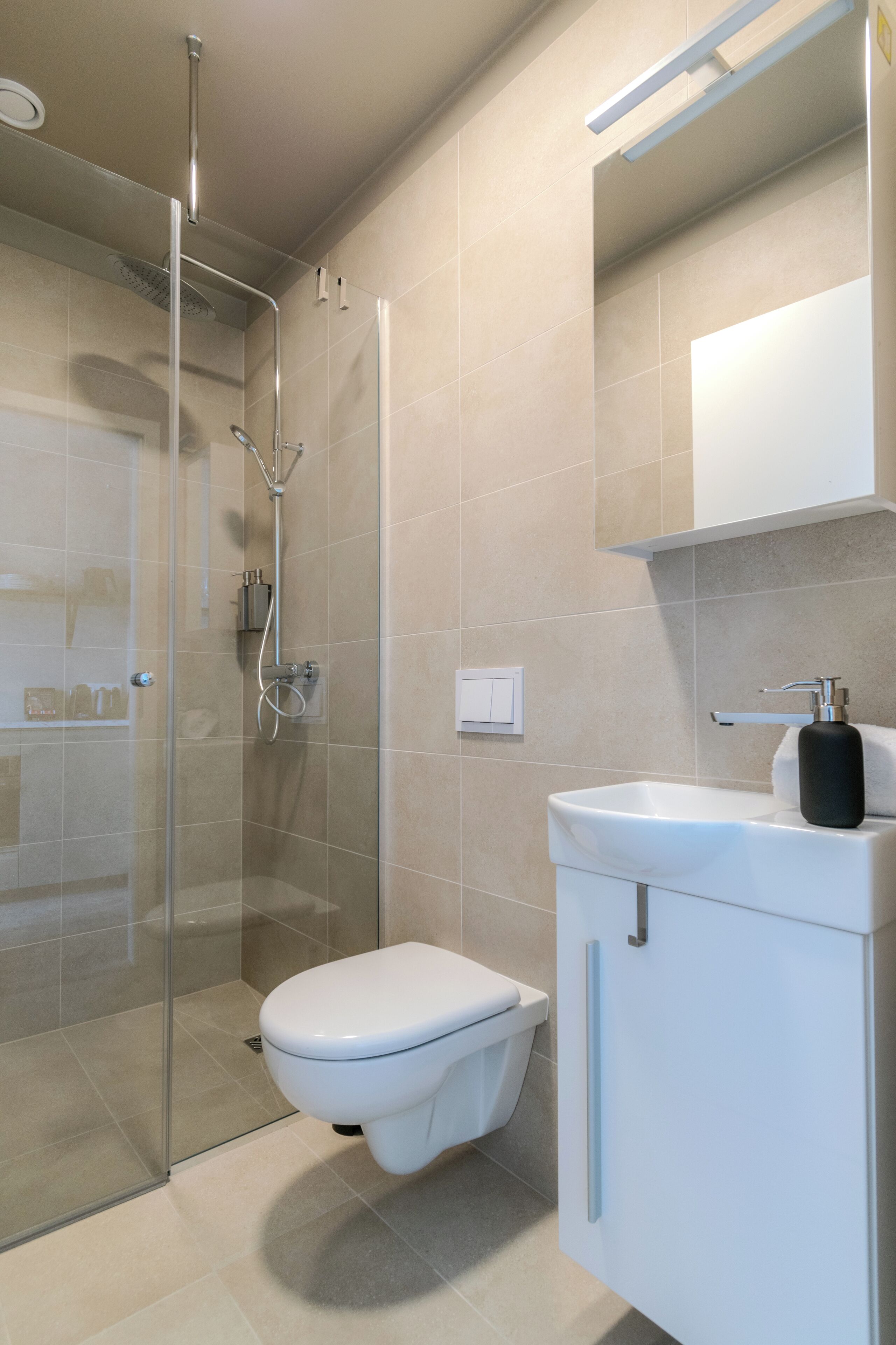 A modern bathroom with a glass-enclosed shower, a white toilet, and a white sink with a black soap dispenser.