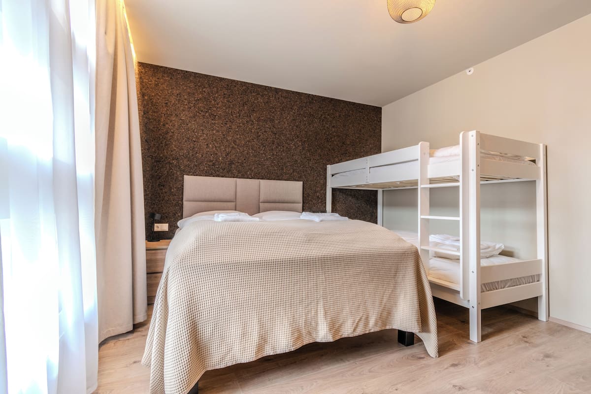 A bedroom with a bunk bed, a large bed with a headboard, and a wooden floor.