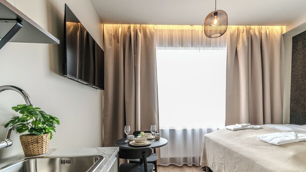 A modern hotel room with a bed, a dining area with a table and chairs, a sink, and a television mounted on the wall. - Frost Apartments by Heimaleiga (Reykjavik)