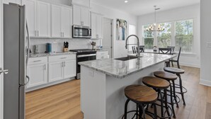 Una cocina moderna con armarios blancos, una isla central con taburetes, microondas integrado y un amplio ventanal con persianas.
