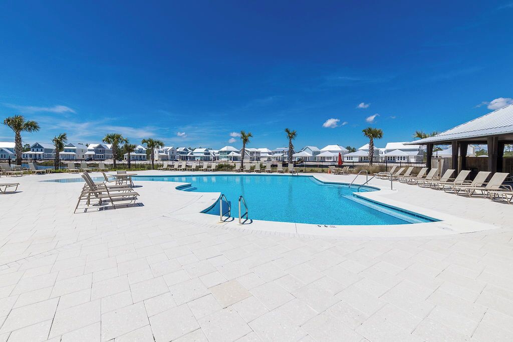 A swimming pool with lounge chairs and palm trees, surrounded by white buildings.