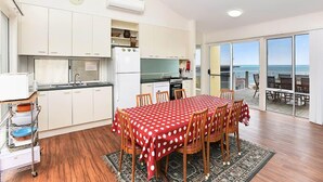 Una cocina compacta con armarios blancos, un refrigerador y un comedor con mantel rojo.