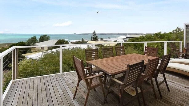 Una terraza de madera con una mesa y sillas, con vista a una playa y al océano.