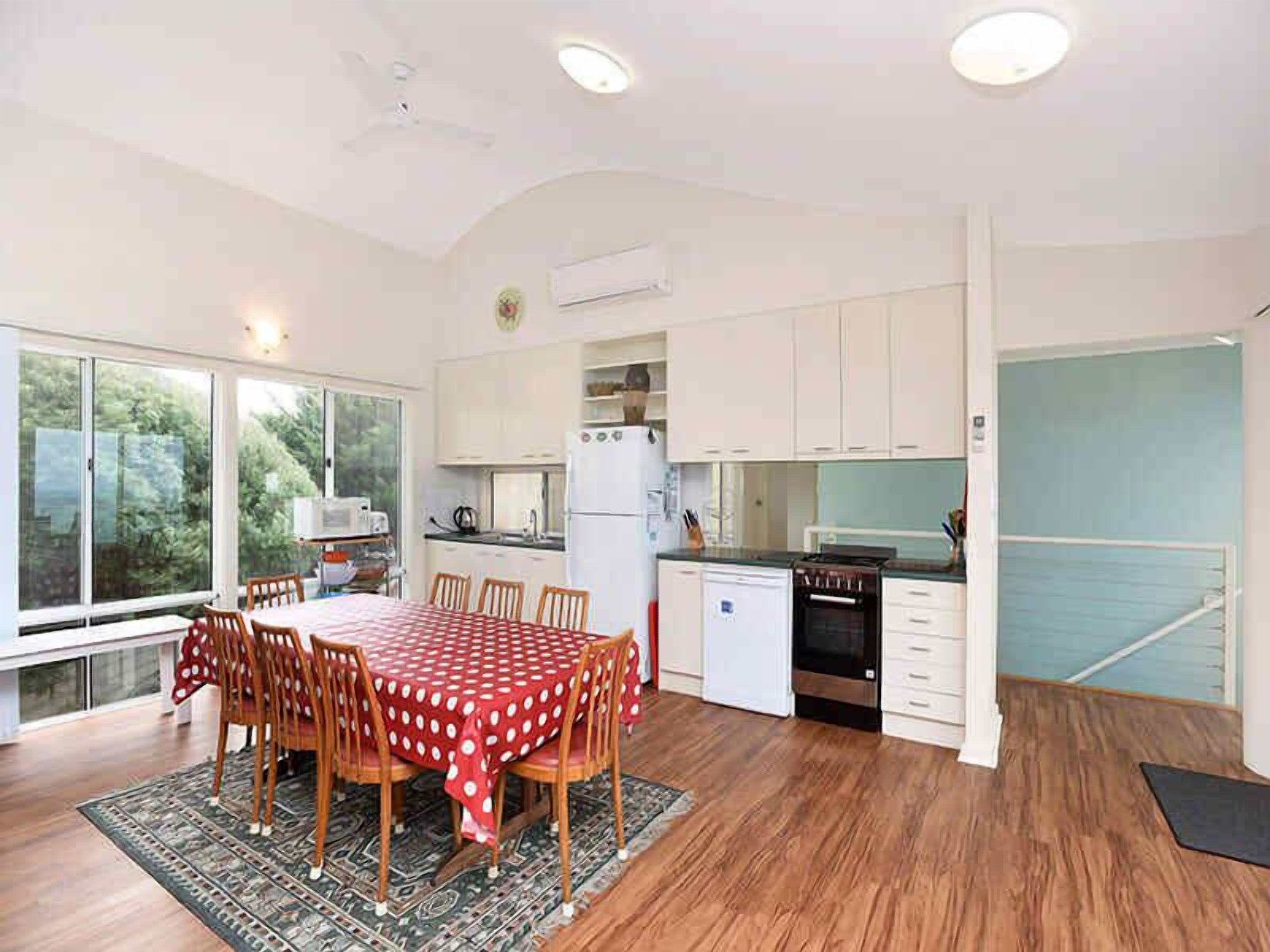 A modern kitchen with white cabinets, a dining table with a red and white checkered tablecloth, and a large window.