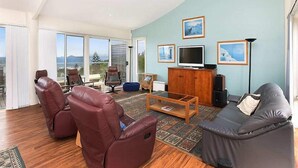 Un salón amplio con un gran ventanal, sillones de cuero, un sofá, un televisor y cuadros enmarcados en la pared.