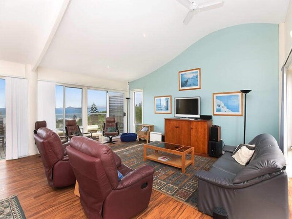 A spacious living room with a large window, leather chairs, a sofa, a television, and framed pictures on the wall. - Boomer Waves, 5 Carfax St - WIFI included (Port Elliot)