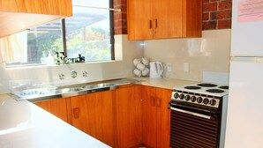 A kitchen with wooden cabinets, a white countertop, a stove, and a window with a view of greenery.
