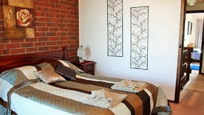A hotel room with a brick wall, two beds with striped bedding, a nightstand with a lamp, and artwork on the walls.