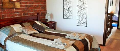 A hotel room with a brick wall, two beds with striped bedding, a nightstand with a lamp, and artwork on the walls.
