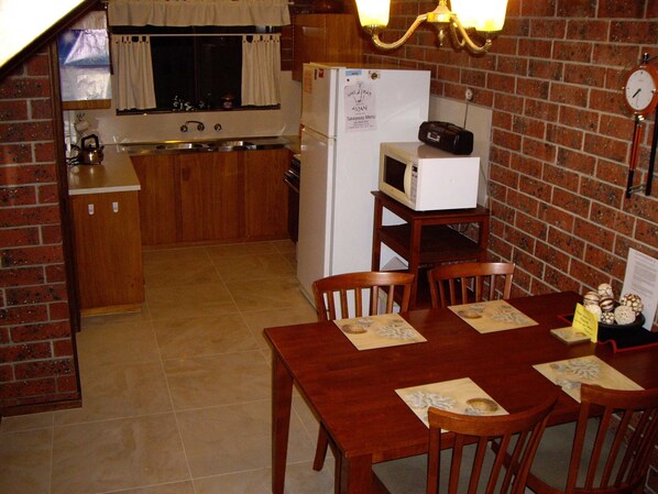 La cuisine est équipée d’un réfrigérateur, d’un four à micro-ondes et d’une cuisinière. On y trouve une table à manger avec des chaises, ainsi qu’une horloge au mur.