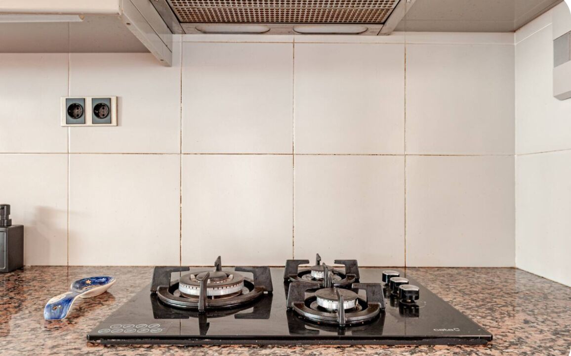 A kitchen with a gas stove, a coffee maker, and two electrical outlets on the wall.