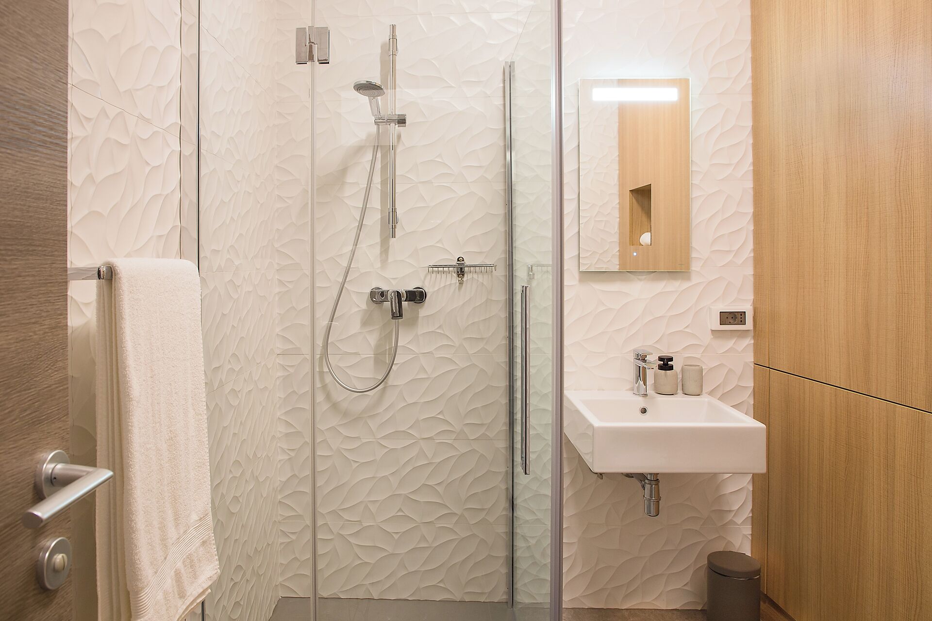A modern bathroom with a glass shower enclosure, a wooden vanity with a mirror, and a white sink.