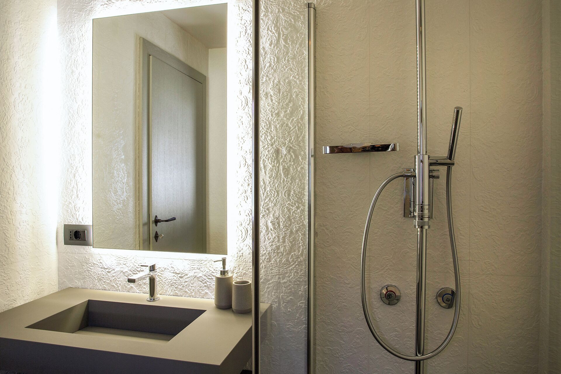 Een moderne badkamer met een glazen douchecabine, een wastafel met spiegel en een structuurwand.