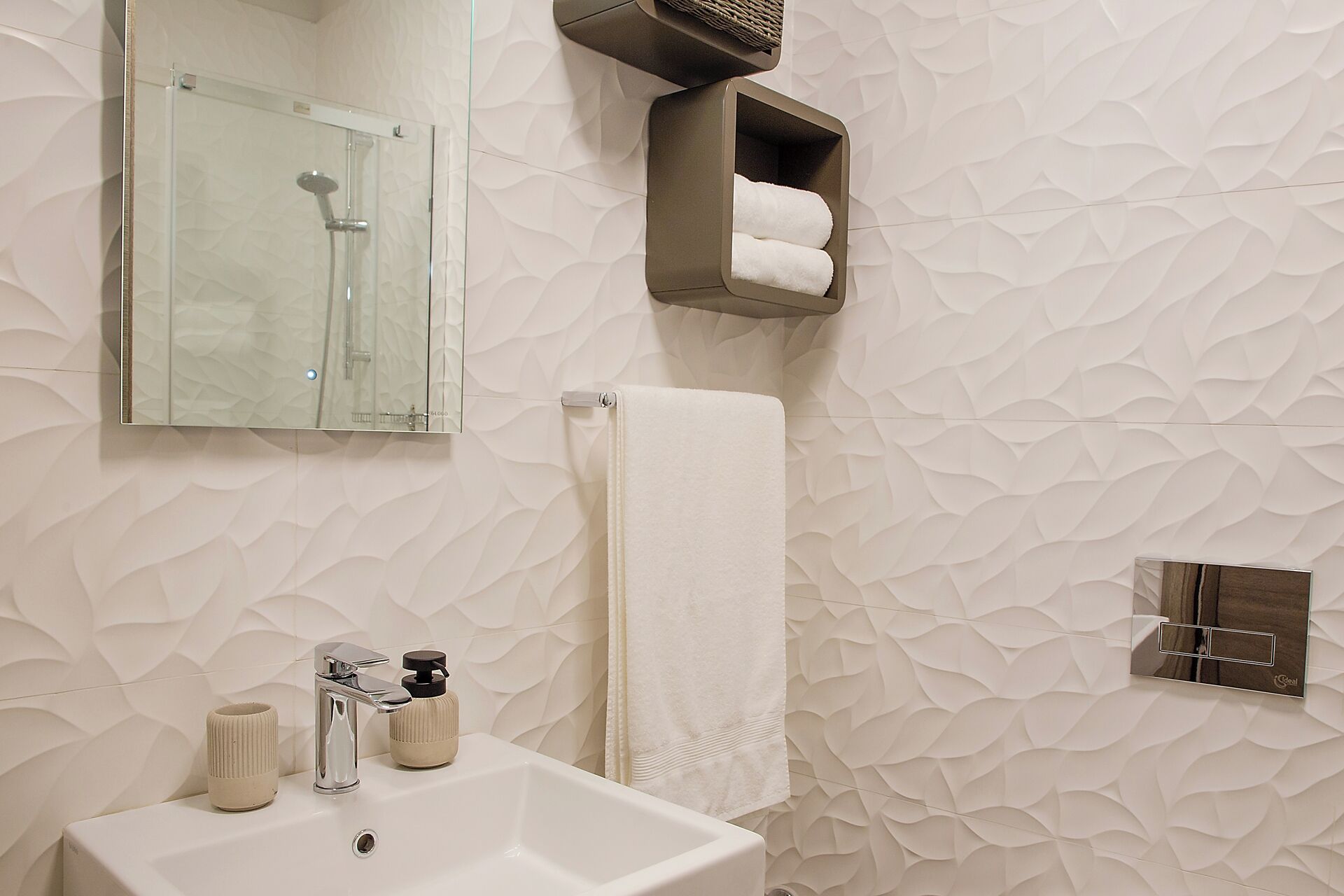 A bathroom with a glass shower enclosure, a white sink, a towel rack, and a towel dispenser.