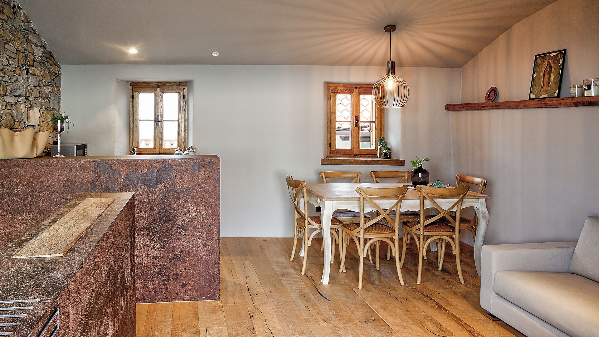 A rustic kitchen with a stone wall, wooden dining table, and chairs.
