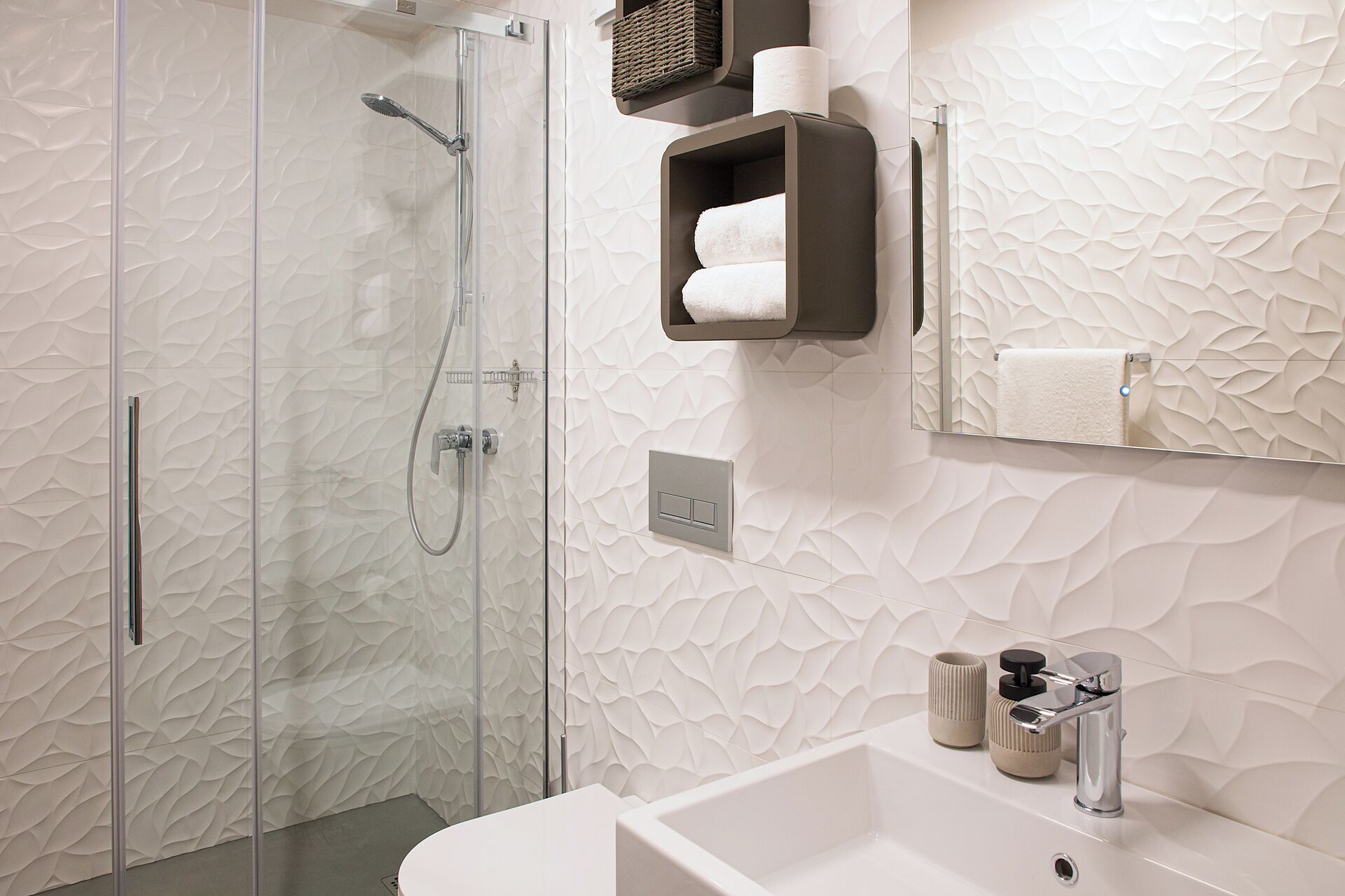 Un baño moderno con cabina de ducha de vidrio, un lavamanos blanco con grifo cromado y un perchero con dos toallas.