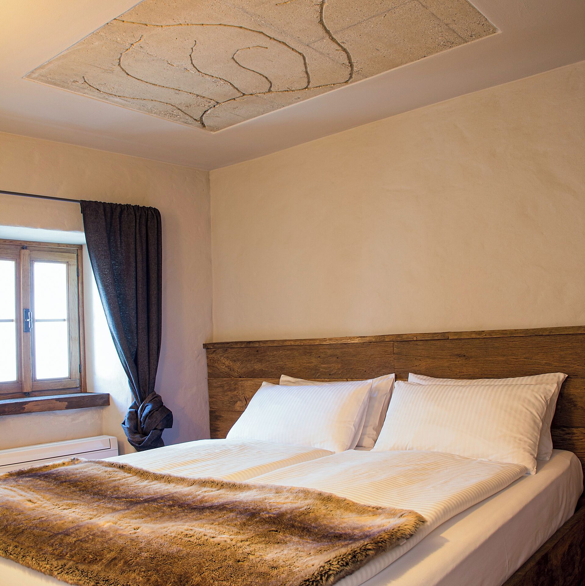 A bedroom with a wooden headboard, white bedding, a fur throw, and a window with curtains.
